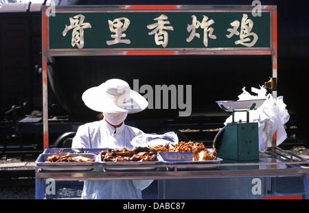 A Chinese vendor wearing a face mask for hygiene selling grilled chicken in a food cart in Zhongwei train station Ningxia province China Stock Photo