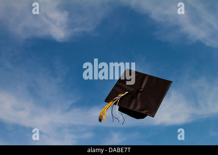 Graduation cap flying through the air at a graduation ceremony against a blue sky with white clouds, Successfully flying free! Stock Photo