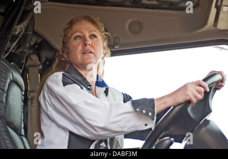Blond woman truck driver checking the road ahead as she drives across country in a semi-truck. Stock Photo
