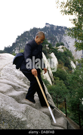 An elderly Chinese man with walking stick descending Hua Shan mountain located near the city of Huayin in Shaanxi province China. Mount Hua is the western mountain of the Five Great Mountains of China, and has a long history of religious significance. Stock Photo