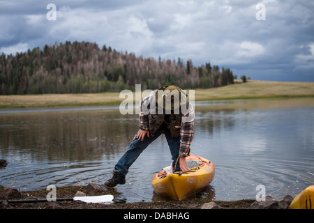 One young caucasian man stepping out of a yellow kayak returning from a fishing trip on Crescent Lake in Arizona..