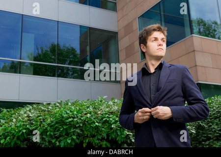 Business man standing in front of office building closing his blazer Stock Photo