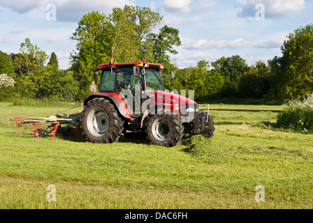 A tractor fitted with grass-cutting attachments cuts grass in a meadow. Stock Photo