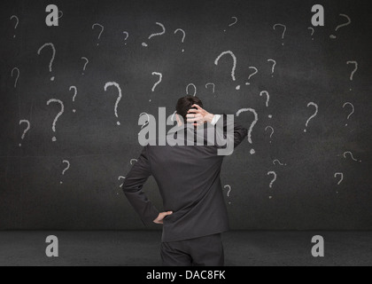 Rear view of a doubtful businessman looking at various question marks Stock Photo