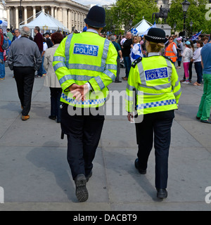 Back view uniformed male and female wpc police officer on foot patrol in high visibility jackets patrolling Trafalgar Square London England UK Stock Photo
