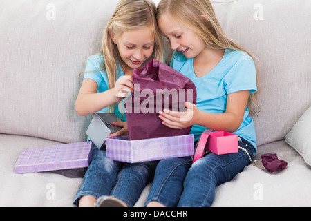 Young twins unwrapping birthday gift sitting on a couch Stock Photo