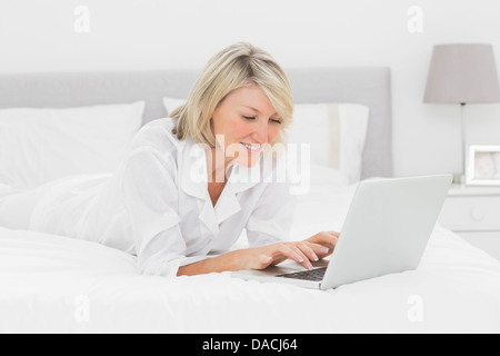 Smiling woman using her laptop on her bed Stock Photo