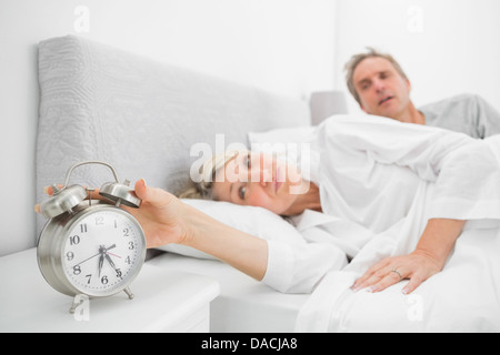 Woman in bed with partner turning off alarm clock Stock Photo