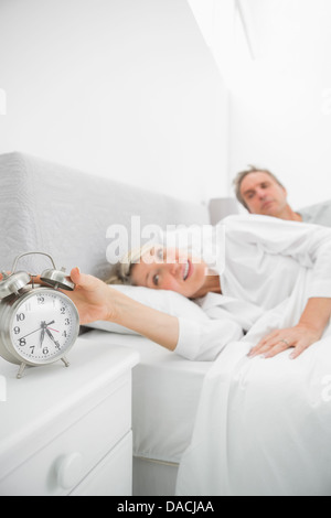 Blonde woman in bed with partner turning off alarm clock Stock Photo
