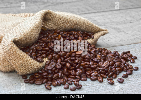 Coffee Beans Spilling from Sack - fresh roast coffee beans spilling from a burlap or jute sack on a rustic background. Stock Photo