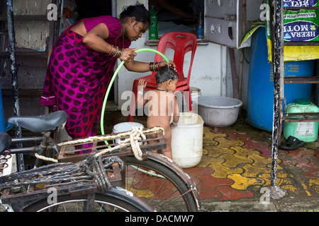 Slum dwellings on Carter Road, Mumbai, small laundry business and home where woman is washing her young child from a bucket Stock Photo