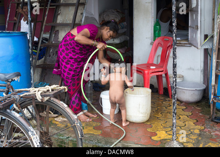 Slum dwellings on Carter Road, Mumbai, small laundry business and home where woman is washing her young child from a bucket Stock Photo