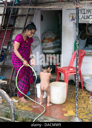 Slum dwellings on Carter Road, Mumbai, small laundry business and home where woman is washing her young child from a bucket Stock Photo