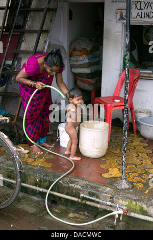 Slum dwellings on Carter Road, Mumbai, small laundry business and home where woman is washing her young child from a bucket Stock Photo