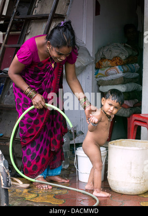 Slum dwellings on Carter Road, Mumbai, small laundry business and home where woman is washing her young child from a bucket Stock Photo