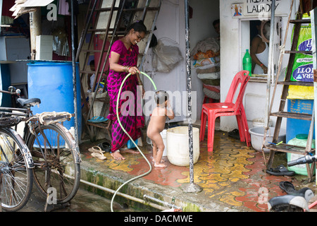 Slum dwellings on Carter Road, Mumbai, small laundry business and home where woman is washing her young child from a bucket Stock Photo