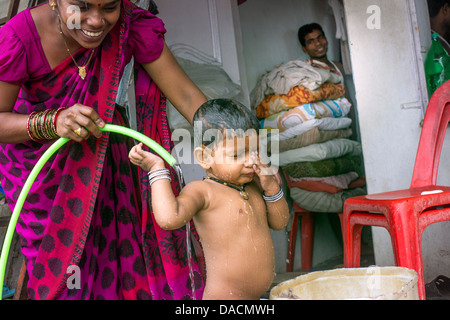 Slum dwellings on Carter Road, Mumbai, small laundry business and home where woman is washing her young child from a bucket Stock Photo