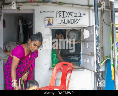 Slum dwellings on Carter Road, Mumbai, small laundry business and home where woman is washing her young child from a bucket Stock Photo