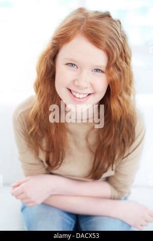 Vertical portrait of a cute red-haired girl sitting and looking at the camera Stock Photo