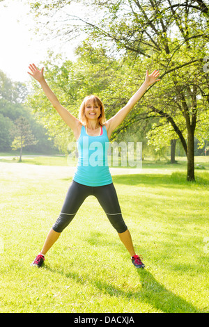 Female fitness instructor doing jumping jacks exercising in green park Stock Photo
