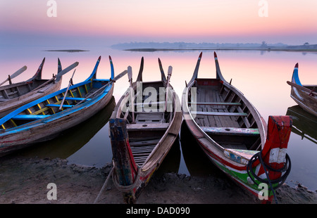 Traditional rowing boat moored on the edge of Taungthaman Lake at dawn, close to the famous U Bein teak bridge, Myanmar Stock Photo