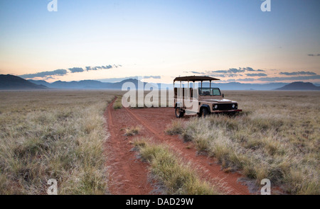 Land rover game vehicle parked by sand road at sunrise, Namib Rand game reserve, Namib Naukluft Park, Namibia, Africa Stock Photo