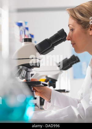 Female microbiologist viewing specimen under microscope in lab Stock Photo