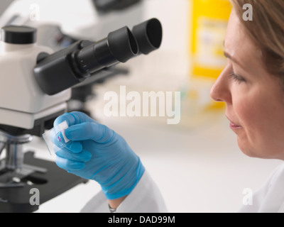 Female microbiologist viewing specimen slide under microscope in lab Stock Photo