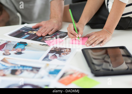 Colleagues making notes on desk of photographs and digital tablet in creative office Stock Photo