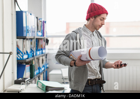 Young office worker holding plans and using mobile phone in creative office Stock Photo