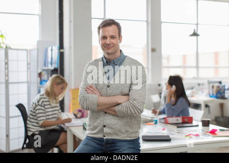 Mature man sitting on desk and smiling in creative office, portrait Stock Photo