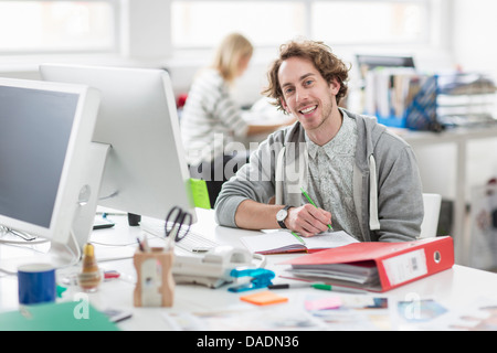 Young man sitting at desk and smiling in creative office, portrait Stock Photo
