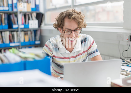 Young man using laptop and smiling in creative office Stock Photo