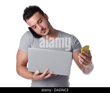 Too much technology. Young man using two mobile phones and one laptop computer, isolated on white Stock Photo