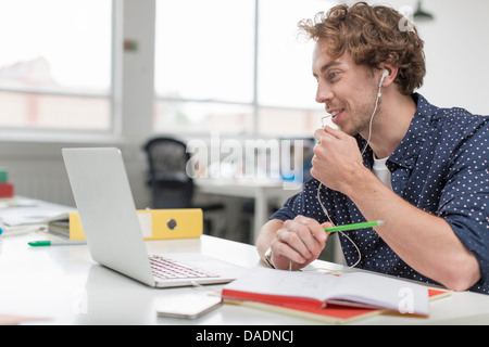 Young office worker using laptop and earphones at desk Stock Photo