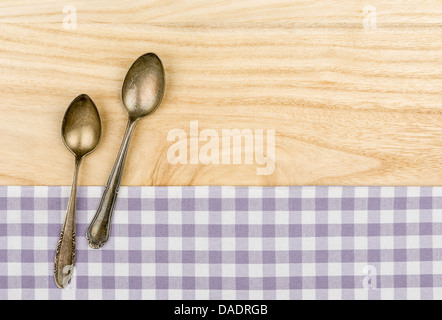 Two silver spoons on a purple checkered table cloth on a wooden background Stock Photo