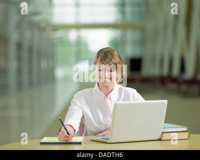 Young student studying taking notes and using laptop, smiling Stock Photo