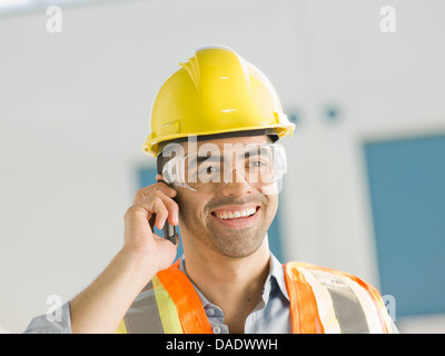 Mid adult construction worker using mobile phone, smiling Stock Photo