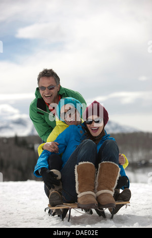 Three friends sitting on sledge in snow Stock Photo