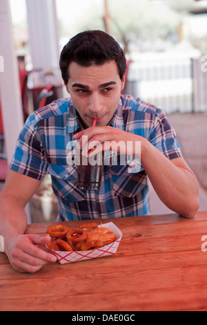 Young man drinking cola in diner, looking away Stock Photo