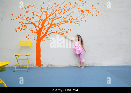 Girl pointing to orange tree mural on wall Stock Photo