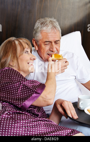 Happy elderly couple having breakfast together in a hotel bed Stock Photo