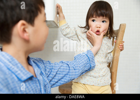 Mischievous brother holding young sisters face Stock Photo