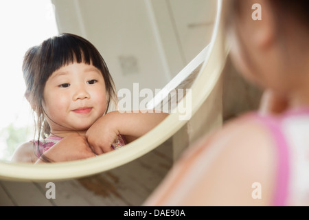 Toddler looking in mirror whilst fastening her dress Stock Photo
