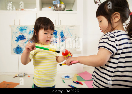 Two young sisters holding paint bottle and brushes Stock Photo