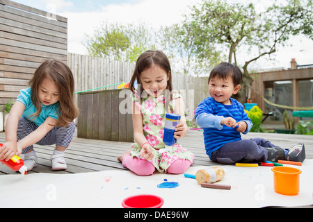 Three young children painting and drawing in garden Stock Photo