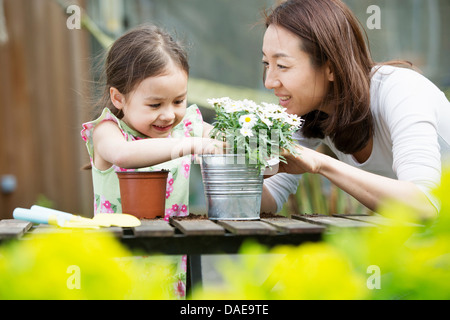 Mother and young daughter potting daisy plant in garden