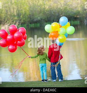 Brother and sister holding balloons in park