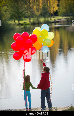 Brother and sister with bunches of balloons in park Stock Photo