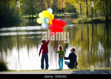 Mother and children in front of lake with bunches of balloons Stock Photo